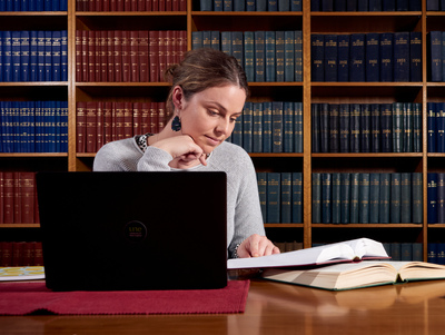 UNE student sitting at desk studies with laptop and textbooks