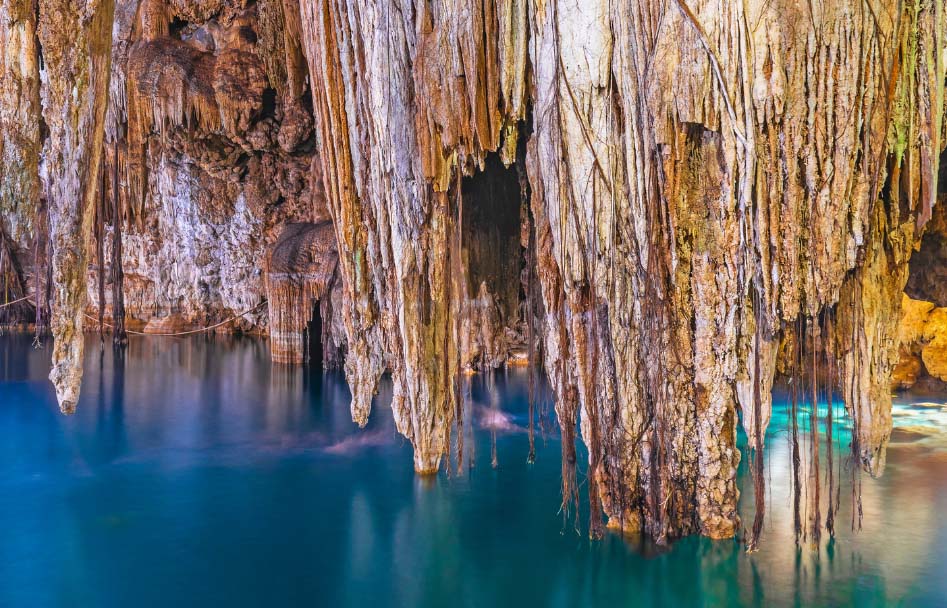 One of the famous underwater caves in Mexico's Yucatán  Peninsula. The image shows a blue pool of water surrounded by rocks and vines.