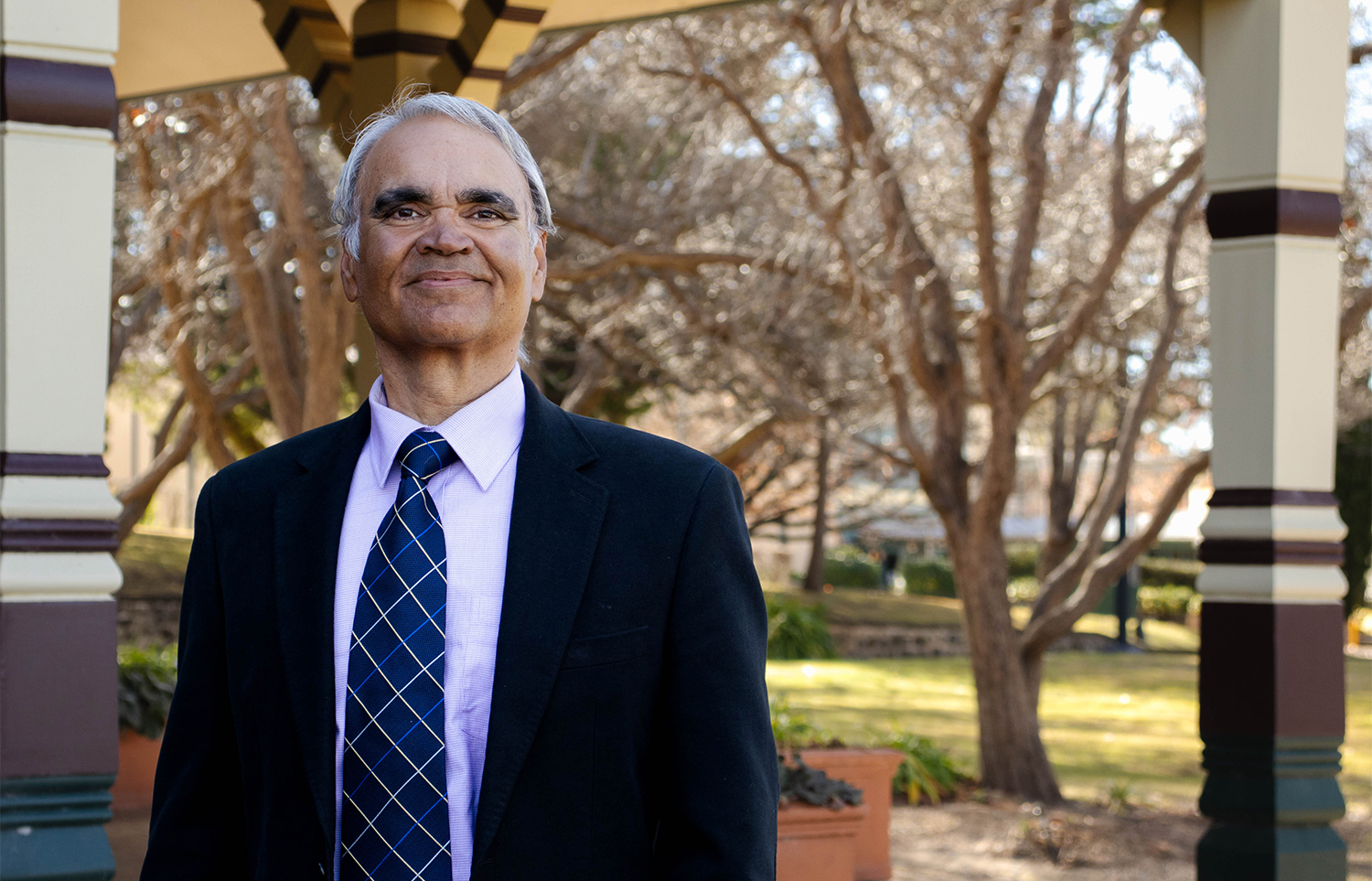 Dr Kamaljeet Sandhu standing in front of the Booloominbah veranda at the UNE Armidale campus.  