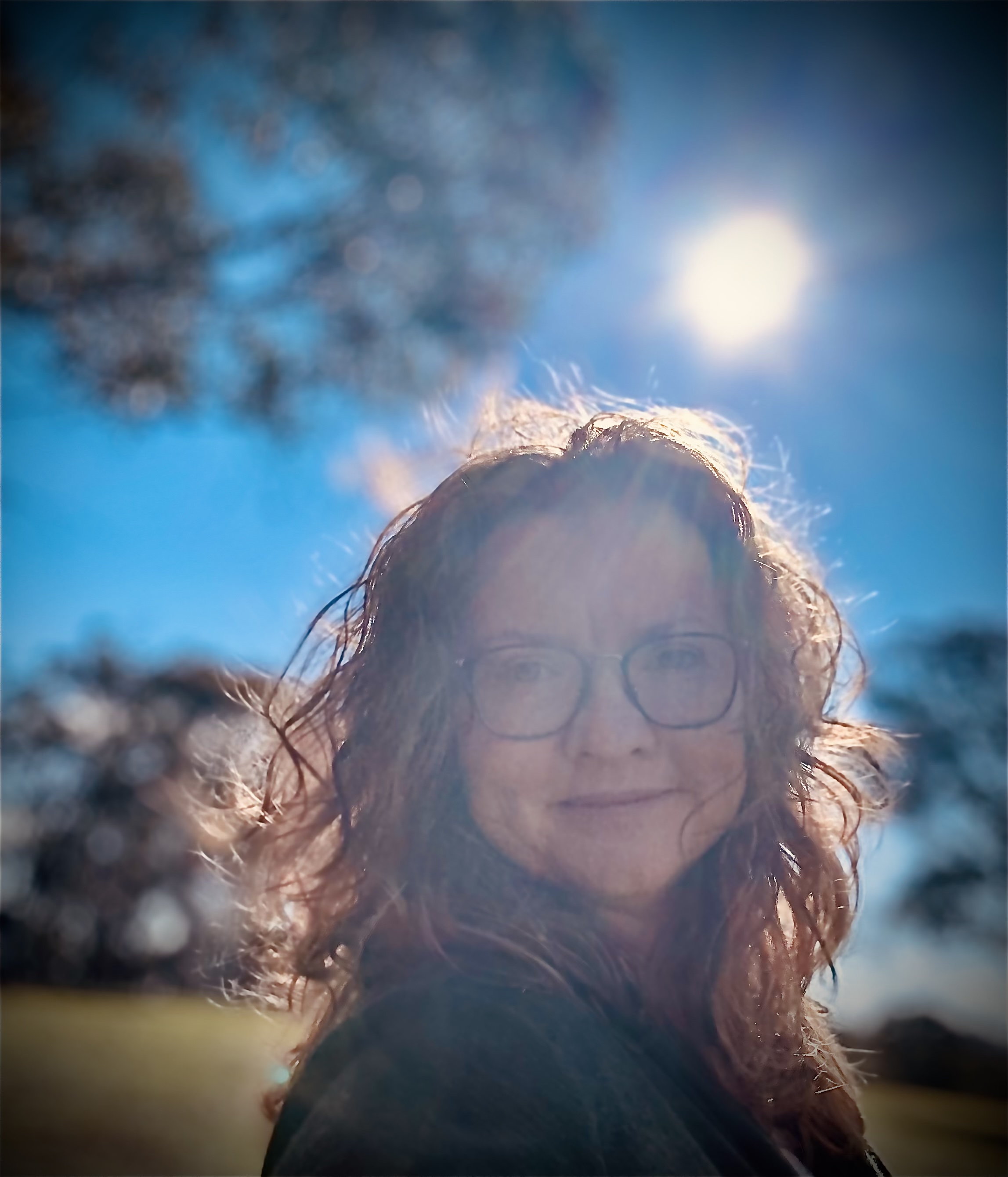 Headshot of a woman with glasses standing in the sun outside.  